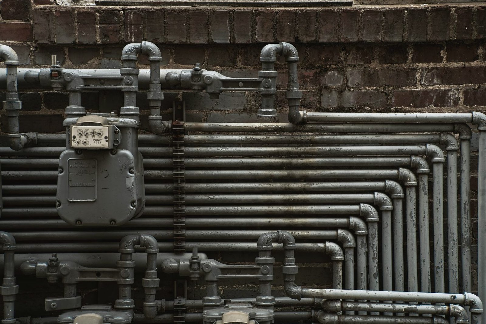 Rows of black iron pipe and a gas meter mounted on an old brick wall