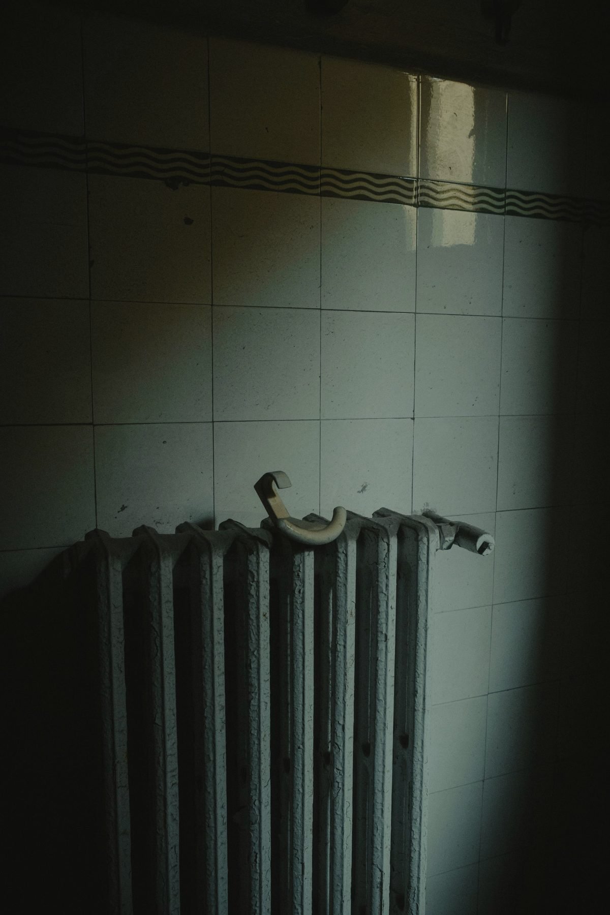 An old column radiator against a tiled wall in low light